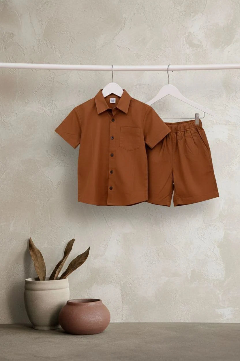 Brown shirt and shorts set on hangers against a beige wall with two pots below.