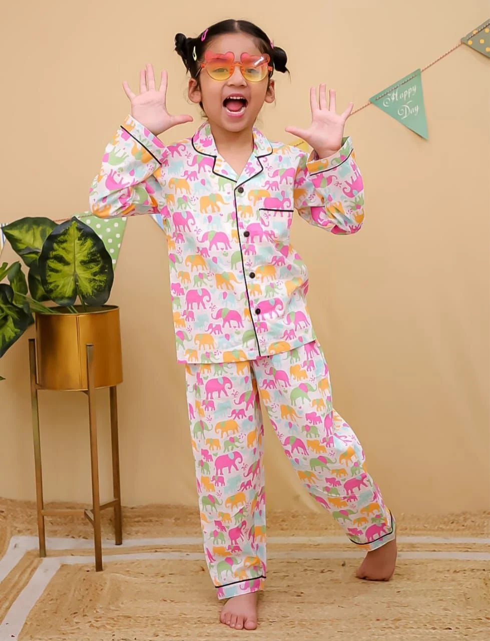 Child wearing colorful pajamas with animal patterns in a room with a plant and decorative items.